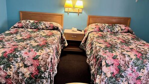 A room with two beds, each with floral bedding, a wooden headboard, a nightstand with a lamp, and a wall-mounted light fixture. - BUDGET INN (Jacksonville)