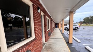 A covered walkway adjacent to a building with large windows and a brick facade. - BUDGET INN (Jacksonville)