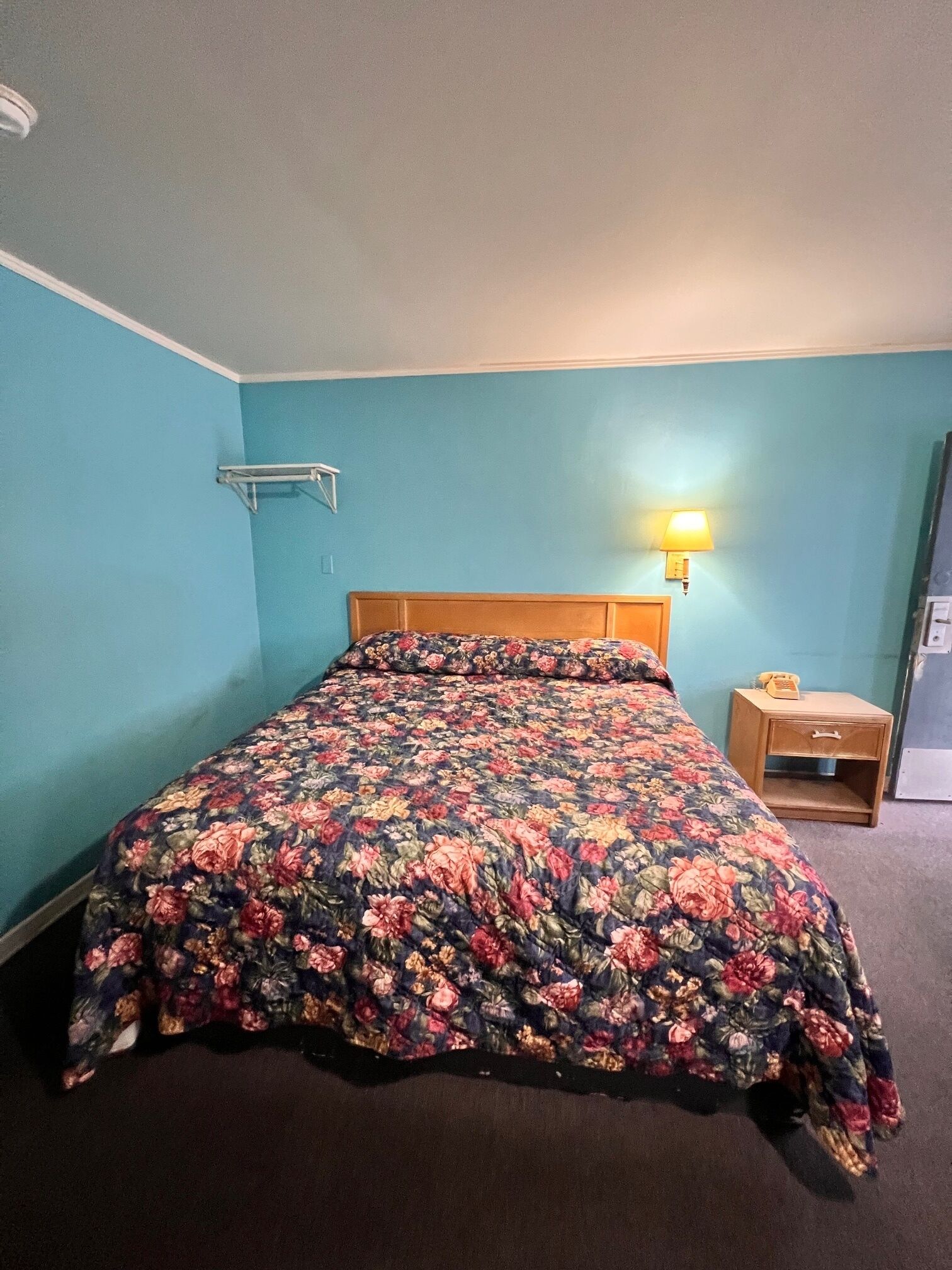 A room with a bed, a nightstand, and a wall-mounted lamp.