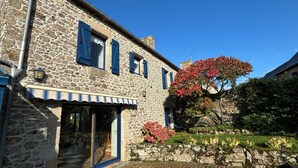 A stone building with a wooden door and blue shutters, surrounded by greenery and a clear sky. - Charming and spacious Breton house (Jugon-les-Lacs)