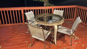 Een ronde glazen tafel met vier stoelen op een houten terras.