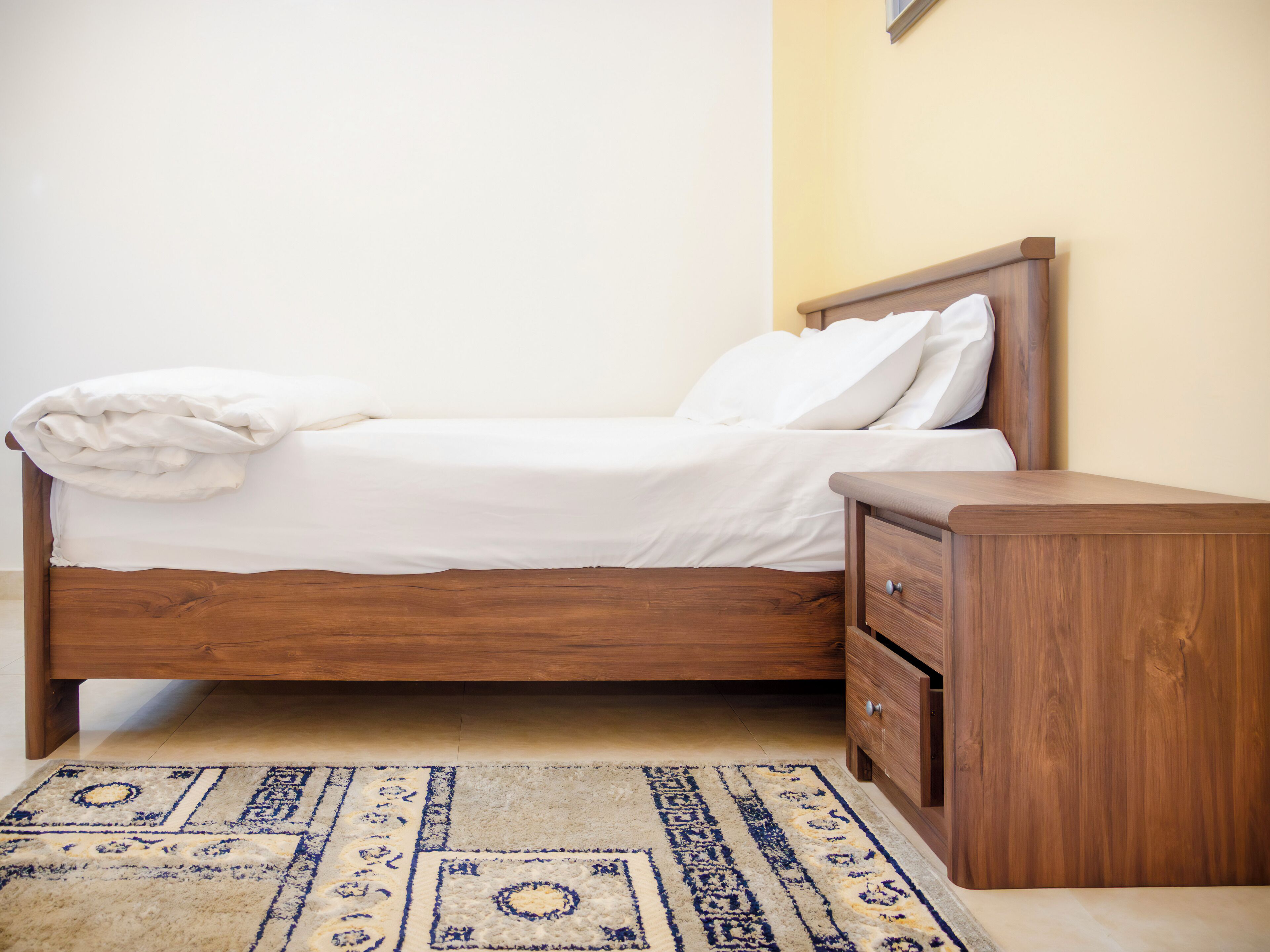 Una cama bien tendida con cabecera de madera y una mesita de noche a juego con cajones.