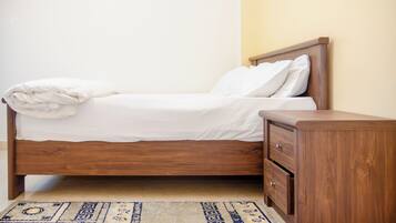 Una cama bien tendida con cabecera de madera y una mesita de noche a juego con cajones.