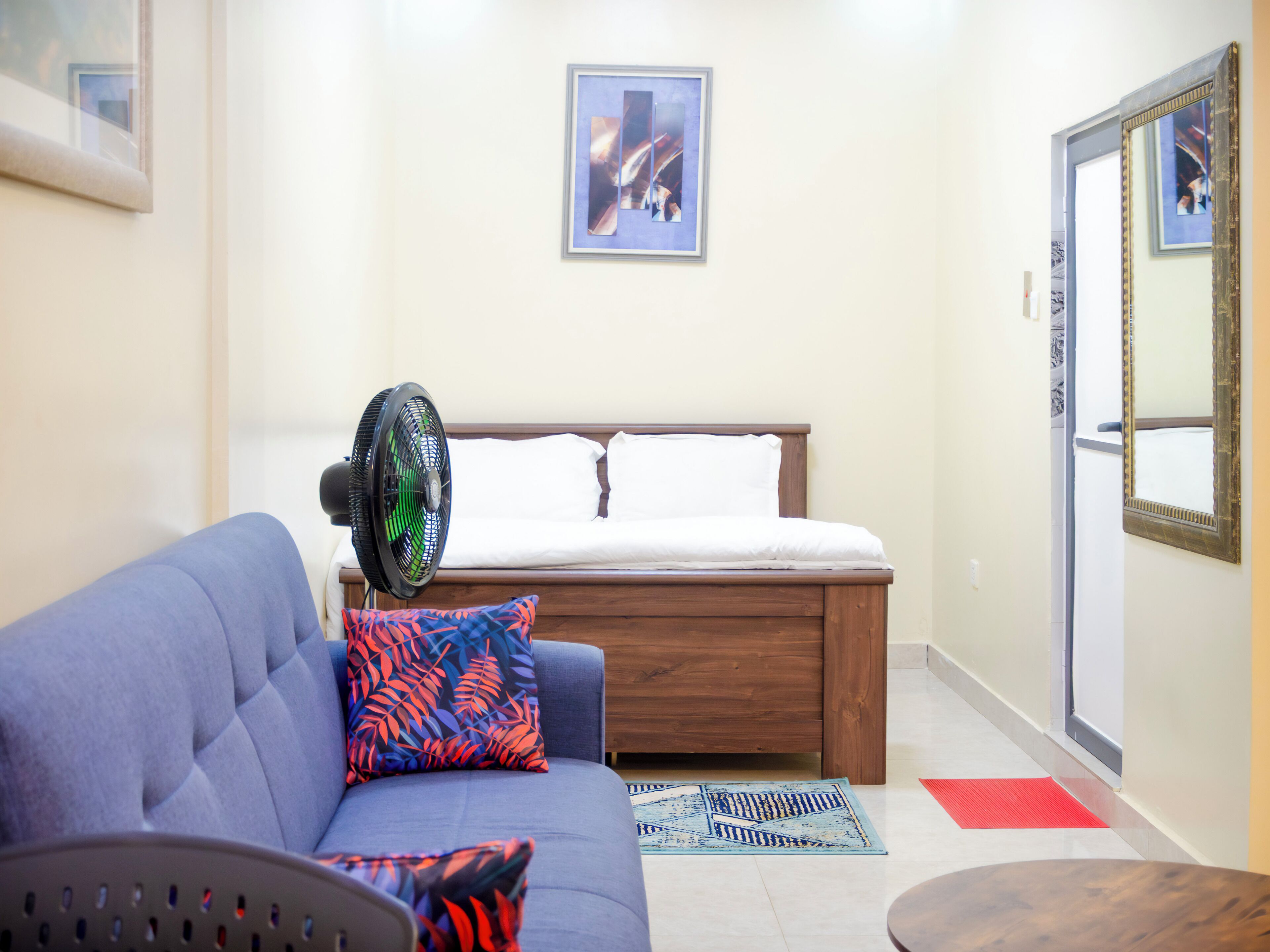 A bedroom with a bed, a blue sofa, a fan, and a small table.