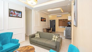 A modern living room with a sofa, two armchairs, and a coffee table. There is a dining area in the background with a table and chairs. - Legacy Apartments Phase 4 (Serrekunda)