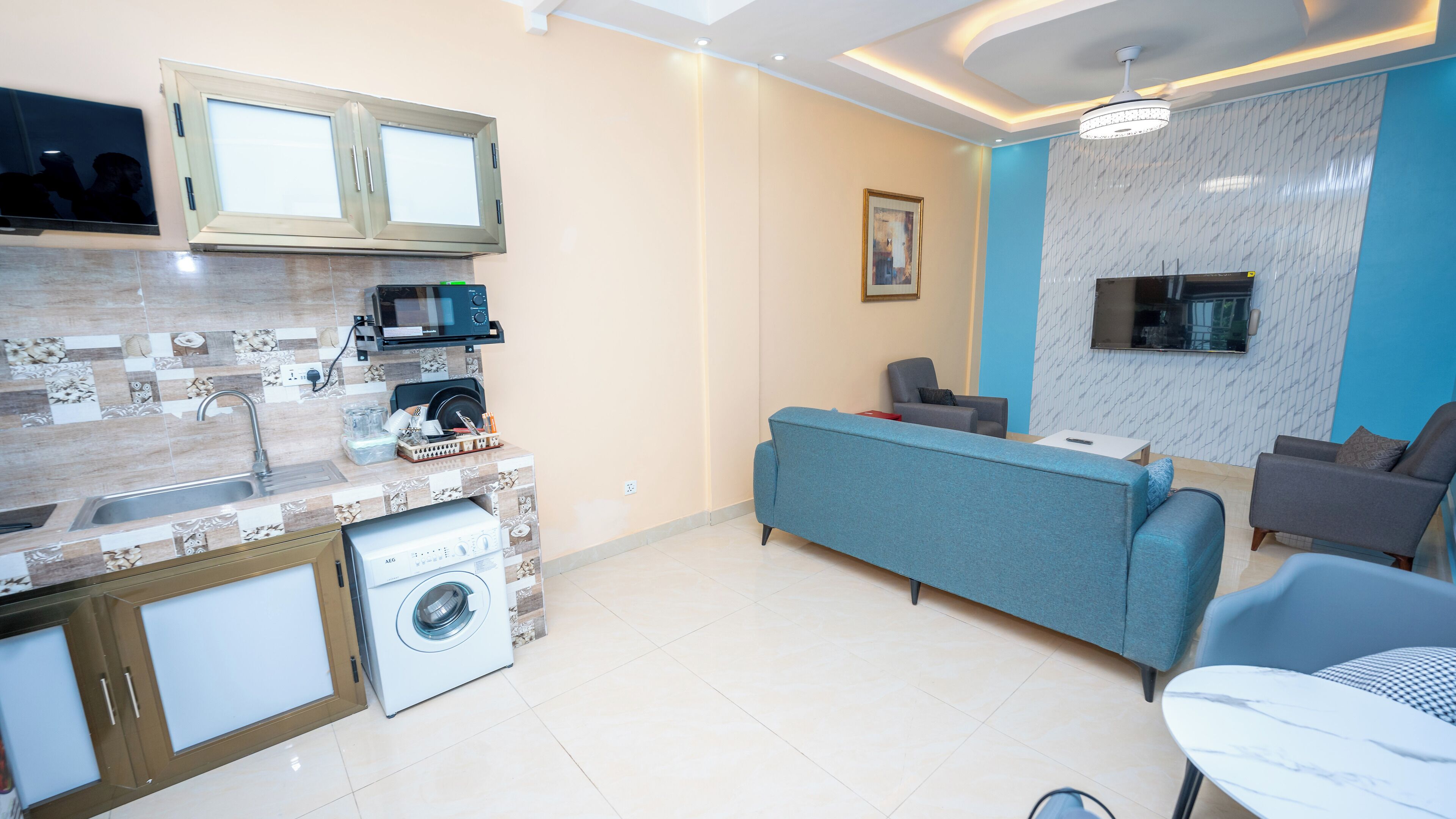 Un salon moderne avec un canapé bleu, des fauteuils gris et un téléviseur fixé au mur.