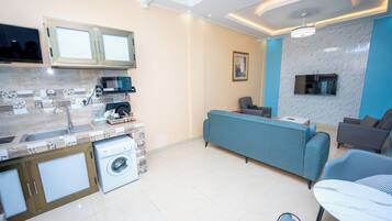 Un salon moderne avec un canapé bleu, des fauteuils gris et un téléviseur fixé au mur.