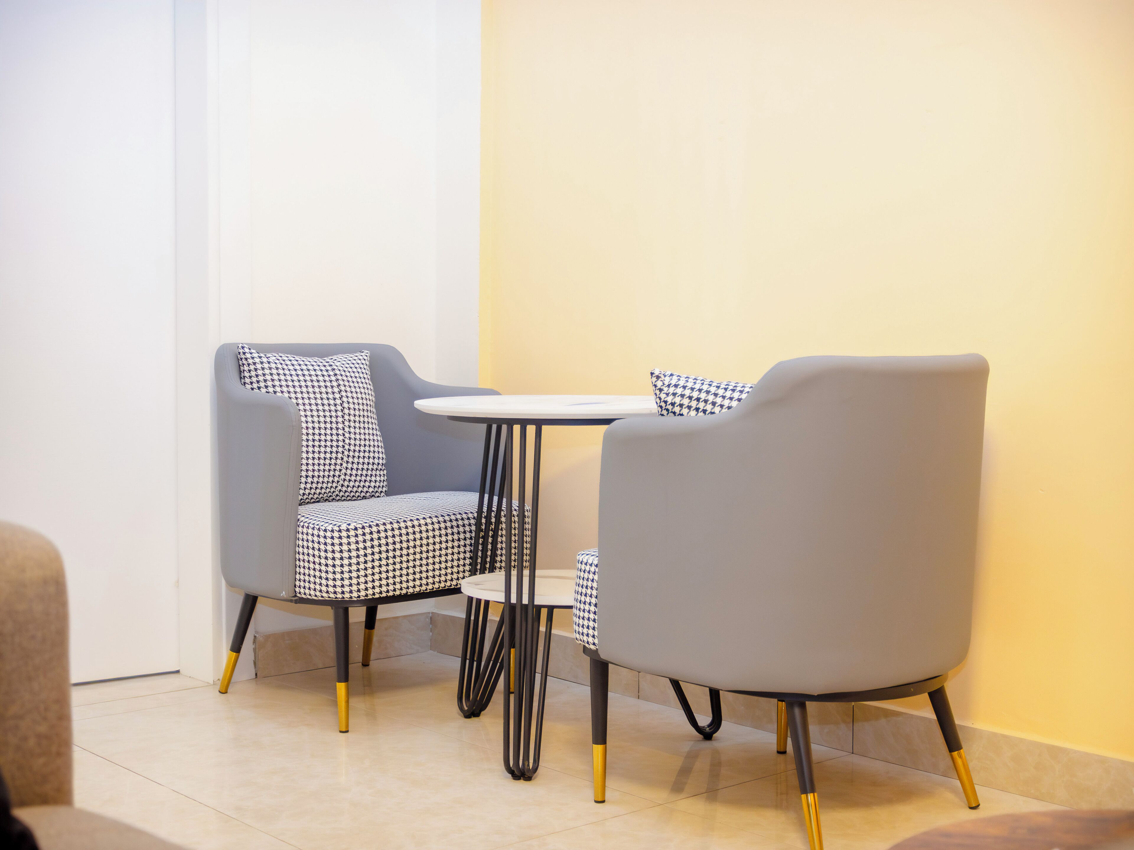A modern dining area with two grey chairs and a small round table, featuring black and white patterned cushions.