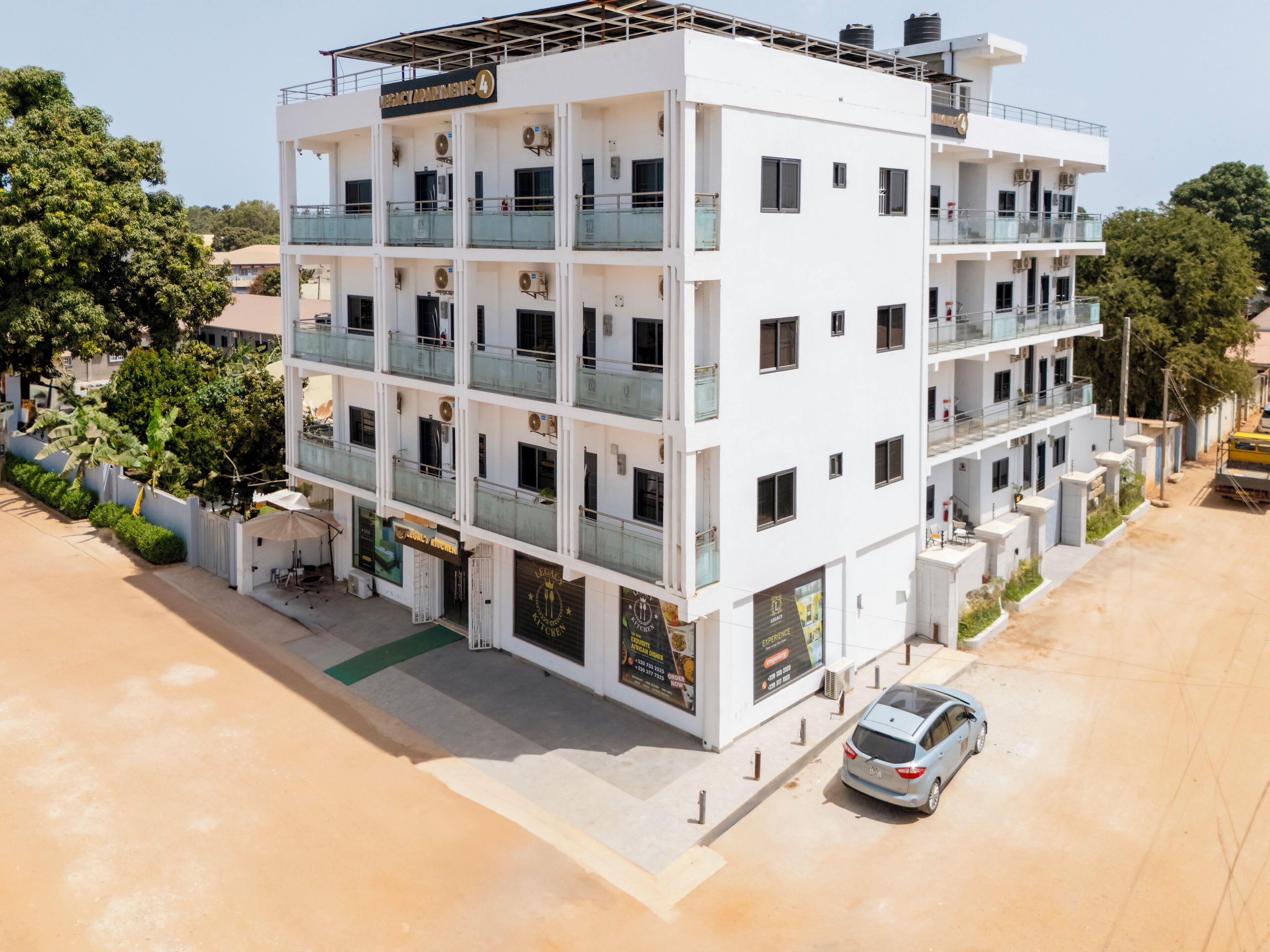 A multi-story hotel with a white facade, balconies, and a parking area.