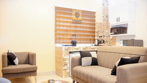 A living room with a sofa, armchairs, and a coffee table. There is a kitchen area with a microwave and a refrigerator. - Legacy Apartments Phase 4 (Serrekunda)