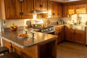 A kitchen with wooden cabinets, a granite countertop, a stove, and a sink. - Cozy lakefront A‑frame w/ hot tub & dock (Decatur)