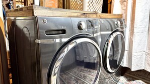 A front-loading GE washer with a control panel, a wooden shelf above it, and a laundry detergent box nearby. - Cozy lakefront A‑frame w/ hot tub & dock (Decatur)