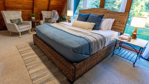 Un dormitorio con una cama grande, dos sillones, una mesita y vistas al exterior con vegetación.