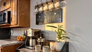 Een keuken met een bordje voor koffie en thee, een koffieapparaat, mokken en een potplant.