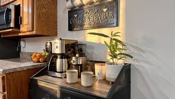 A kitchen with a coffee and tea bar sign, a coffee machine, mugs, and a potted plant.