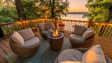 A deck with wicker furniture, a fire pit, and a view of a body of water.