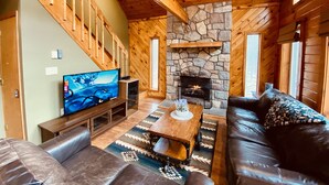 A cozy living room with a stone fireplace, wooden walls, a television, and leather sofas.