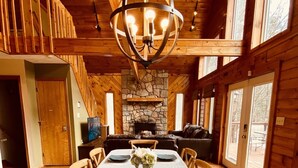 A dining area with a long table set for six, a stone fireplace, and wooden walls.