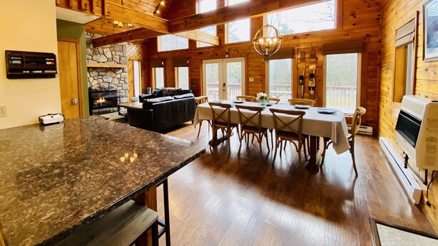 A spacious kitchen with a stone fireplace, wooden ceiling, and large windows.
