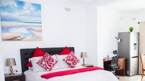 A hotel room with a bed, a desk, a chair, a refrigerator, and a painting on the wall.