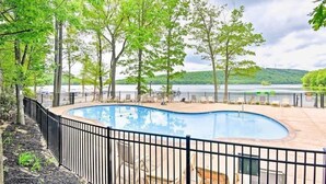 A swimming pool with a curved edge, surrounded by a black metal fence, and trees in the background.
