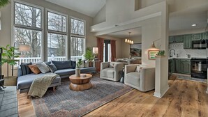 A spacious living room with a large window, a fireplace, and a kitchen area visible through an open door.
