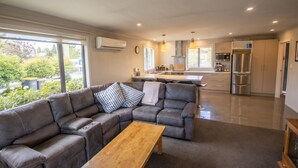 A modern living room with a sectional sofa, a wooden coffee table, and a view of a kitchen with a stainless steel refrigerator and a dining area. - Ultimate Escape in Twizel (Twizel)