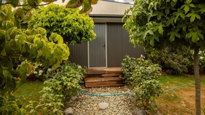 A garden with a wooden deck leading to a grey door, surrounded by various shrubs and a gravel path. - Ultimate Escape in Twizel (Twizel)