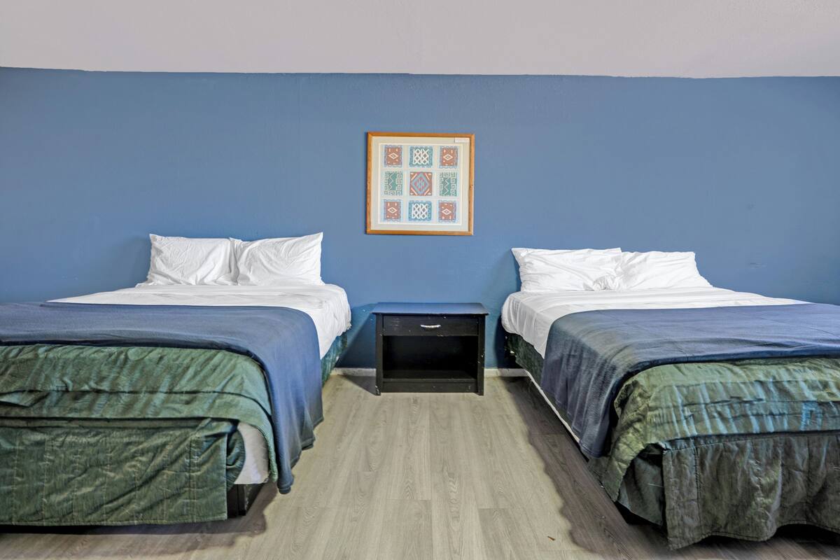 A room with two beds, a small bedside table, and a wall-mounted picture.