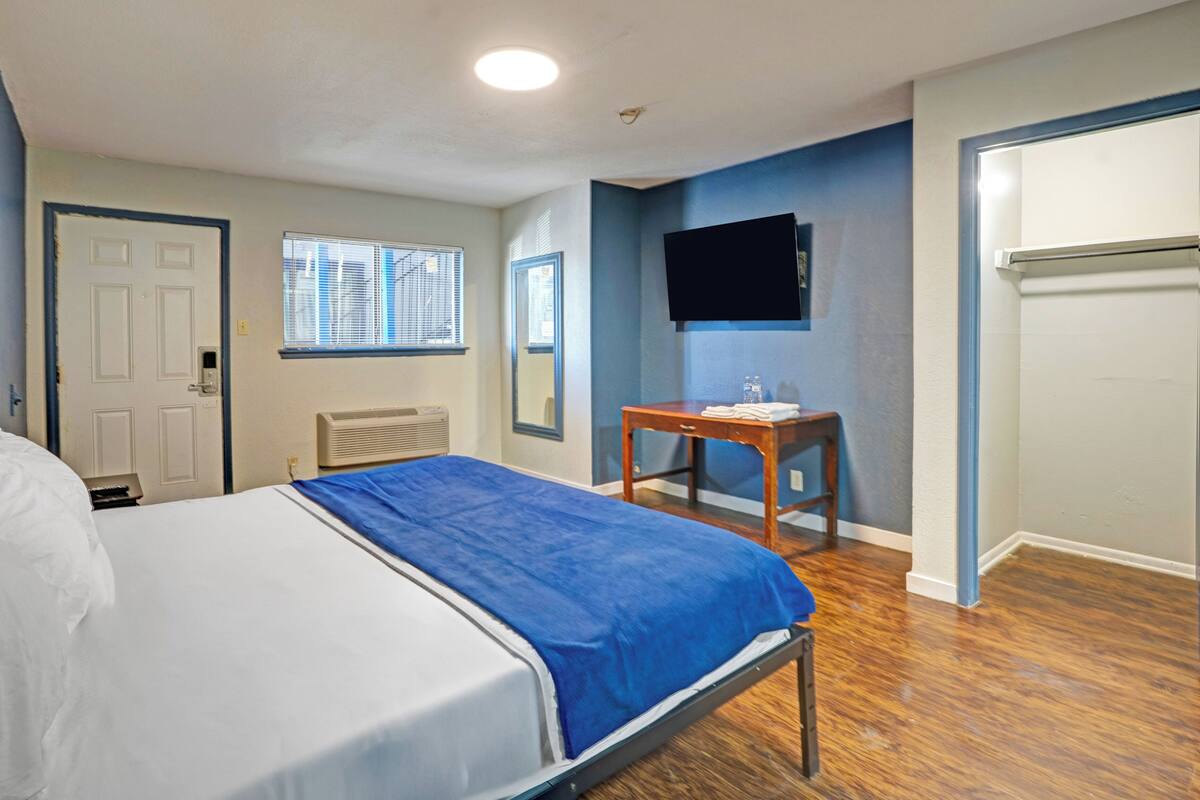 A hotel room with a bed, a desk, a chair, a television, and a window with blinds.