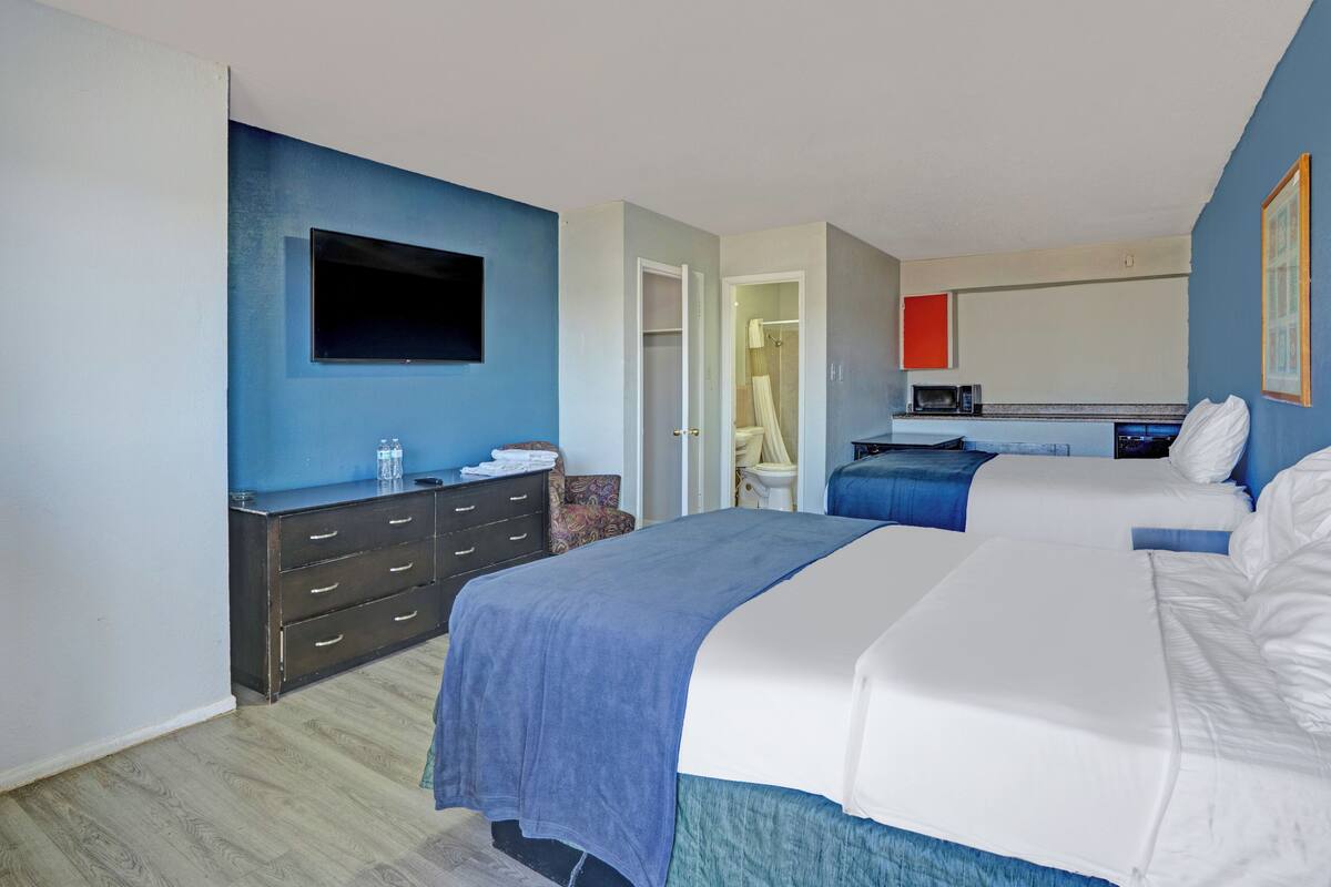 A hotel room with two beds, a TV, a dresser, and a microwave.