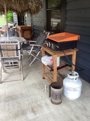 A patio with a grill, a gas cylinder, and a table with chairs.