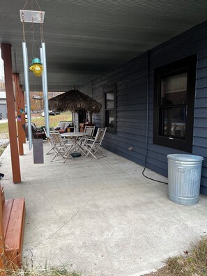 A covered patio area with a table and chairs, a trash can, and a thatched structure.