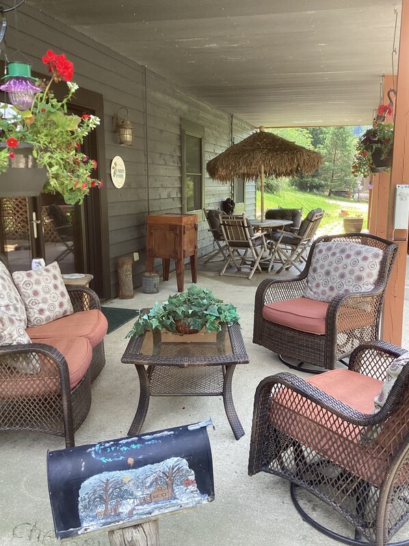 A covered outdoor seating area with wicker furniture, a table with a plant, and hanging flower baskets.