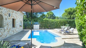 Una piscina con muretto in pietra, lettini e ombrellone.