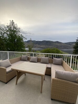 A covered outdoor seating area with wicker furniture and cushions, overlooking a body of water and hills. - Blue Shore Resort (Savona)