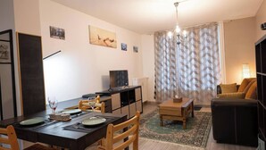 A modern living room with a dining area, a sofa, a TV, and a patterned curtain. - Écrin de Lumière in Vienna (Vienne)