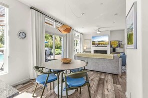 Un salon moderne avec une table ronde, des fauteuils bleus rembourrés, un saladier en bois et un canapé gris.