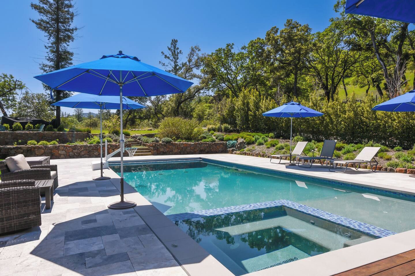 A swimming pool with a stone deck, surrounded by lounge chairs and umbrellas.