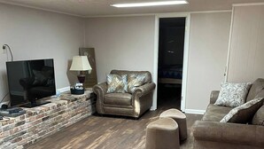 A living room with a brick accent wall, a leather armchair, a sofa, and a television.