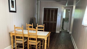 A dining area with a wooden table and chairs, a framed picture on the wall, and a hallway leading to a bathroom.