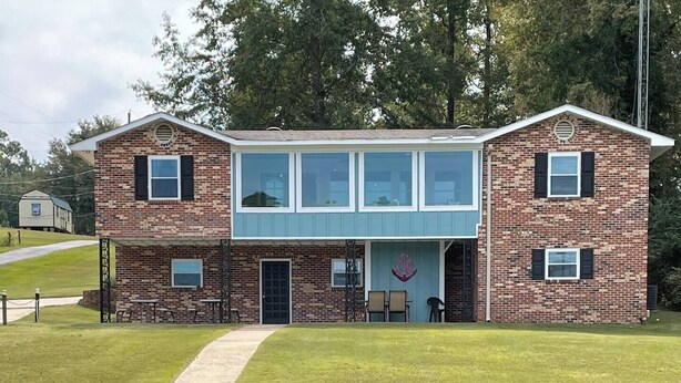 A two-story brick building with a flat roof, a front door, and a small porch area with chairs.