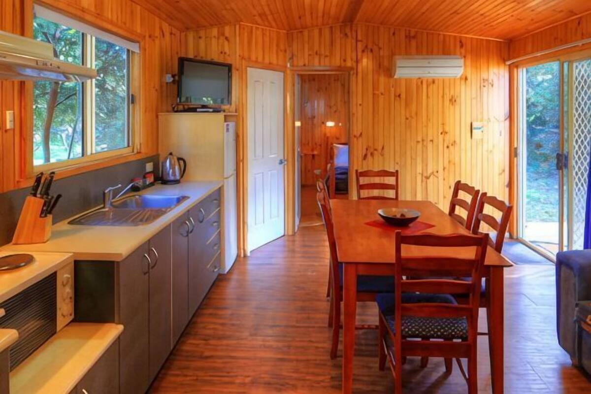 A wooden cabin interior with a kitchen, dining area, and a TV mounted above the counter.
