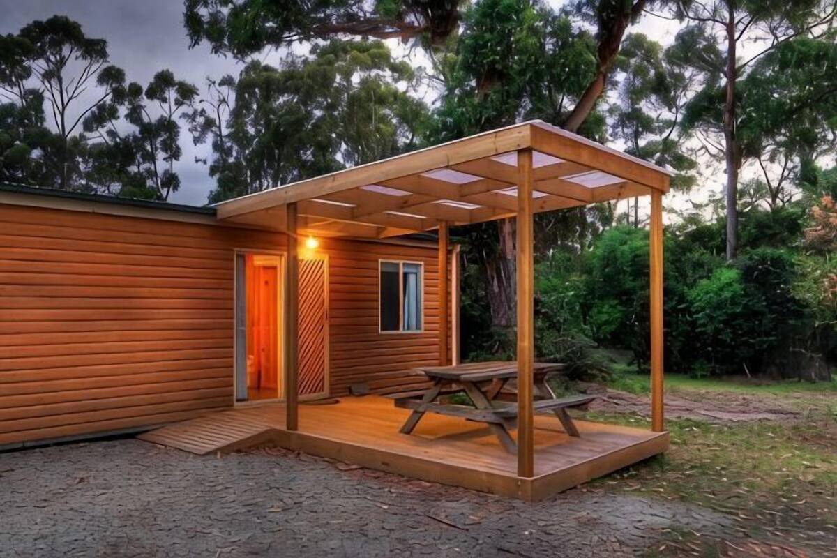 A wooden cabin with a covered patio, a door, and a window.