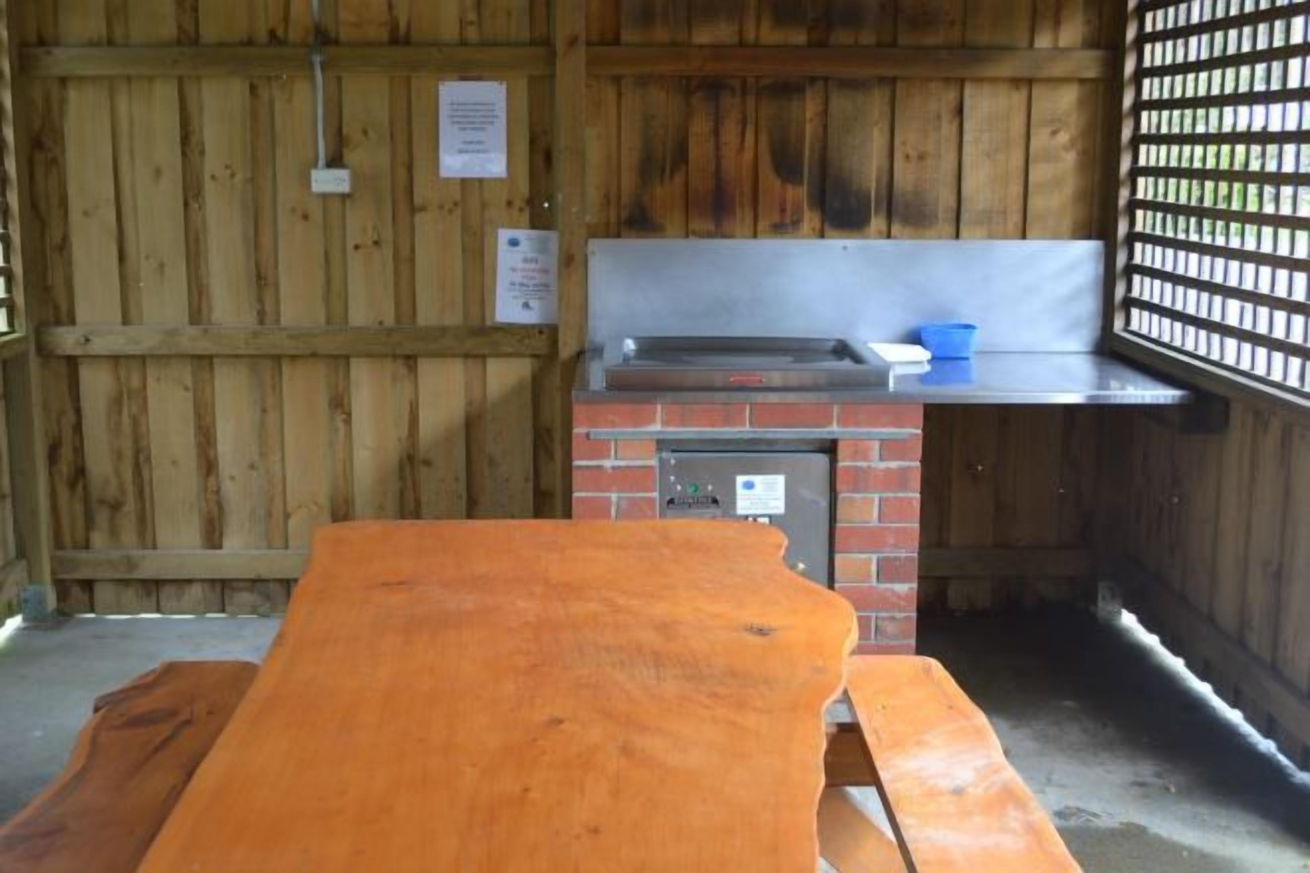 A wooden cabin with a brick stove, a sink, and a picnic table.