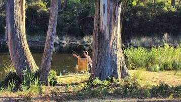 A person fishing by a calm river surrounded by tall trees.