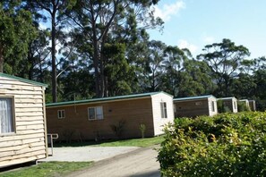A row of wooden mobile homes with a dirt path leading to them, surrounded by trees. - Bruny Island Holiday Park Adventure Bay (Adventure Bay)