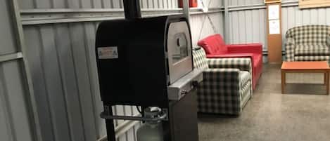 A room with a portable grill, a checkered sofa, a red chair, and a small table.