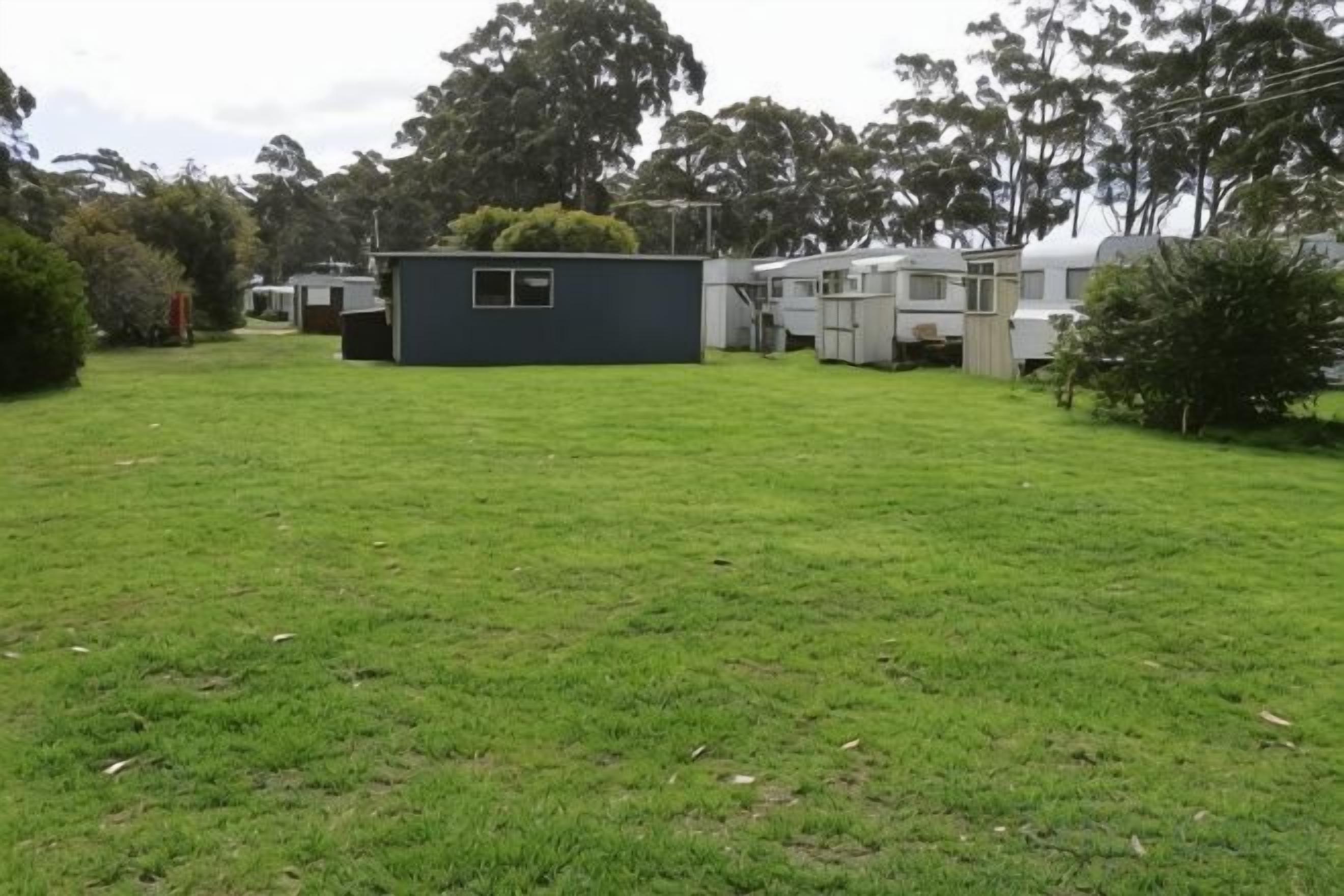 A grassy area with a small building and RVs in the background.