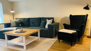A modern living room with a green sofa, a wooden coffee table, a black armchair, and a floor lamp. - 1.5-room apartment with terrace (Pirna)